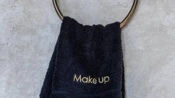 Et mørkeblåt håndklæde med 'Make up' broderet i guld, hængende på en messinghåndklædering.