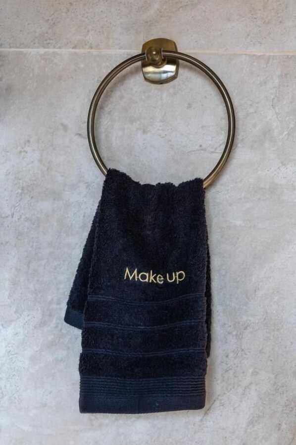 A dark blue towel with 'Make up' embroidered in gold, hanging on a brass towel ring.