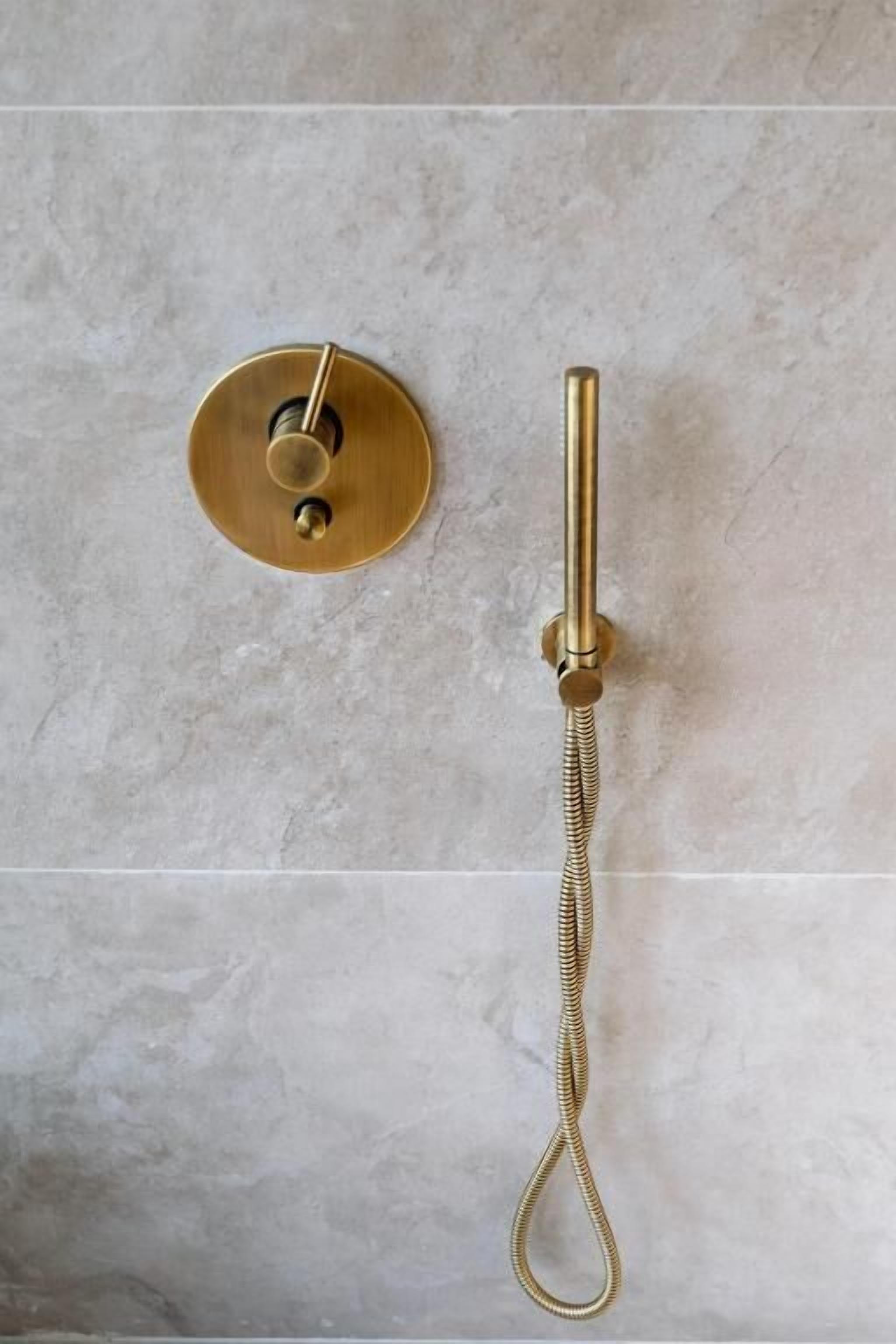 A bathroom with a gold-colored shower control and a handheld showerhead.