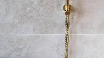 A bathroom with a gold-colored shower control and a handheld showerhead.