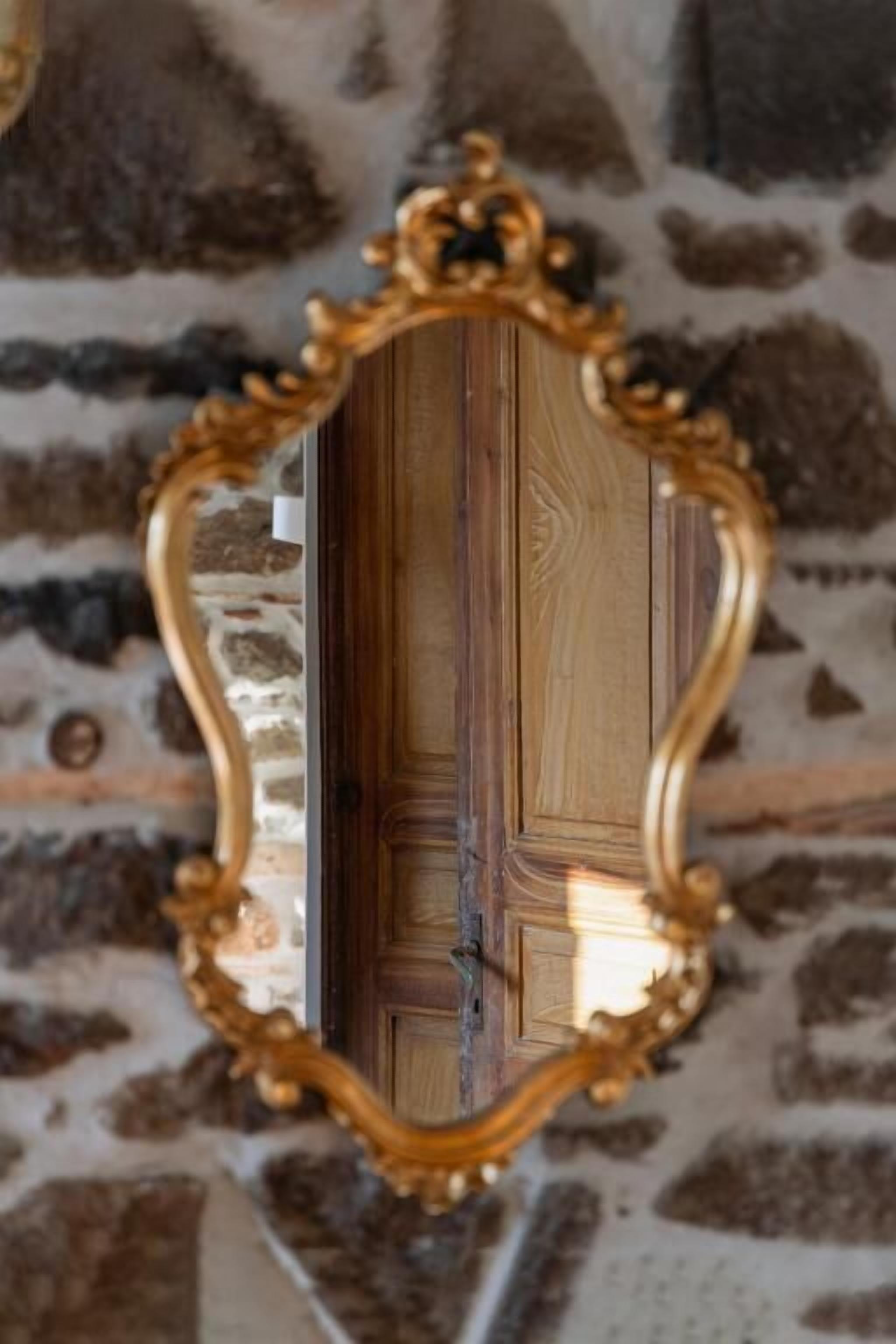Un espejo con un marco dorado ornamentado frente a una pared de piedra.