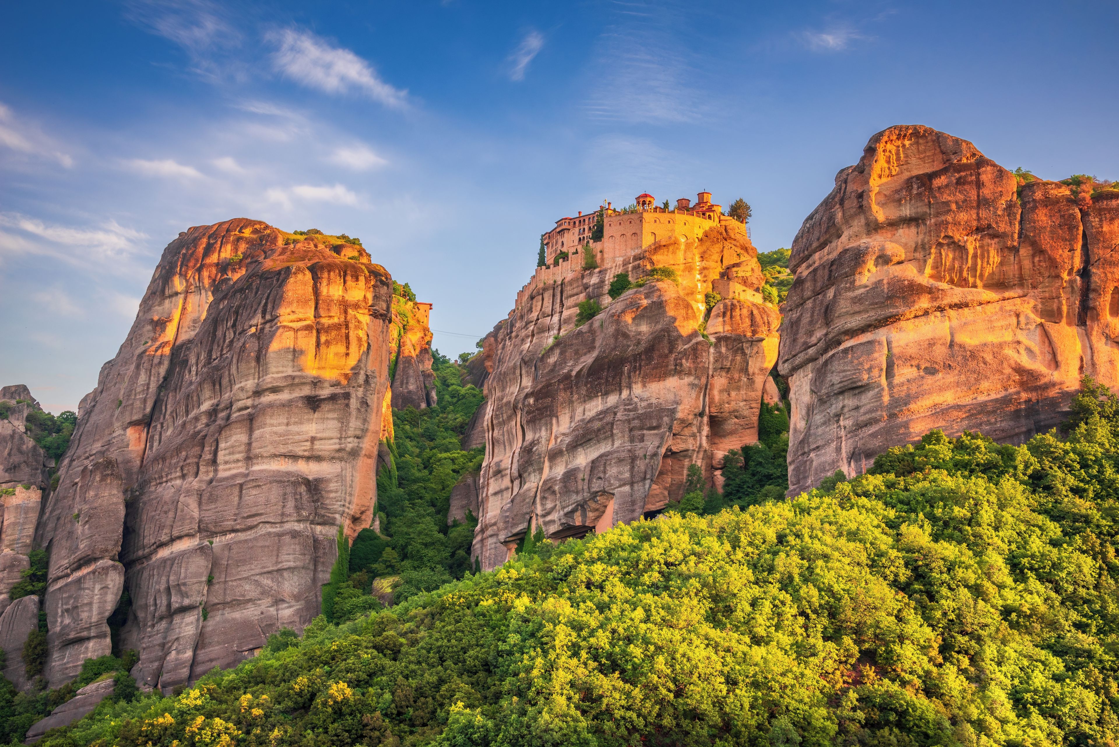Paisagem montanhosa com formações rochosas imponentes e uma floresta densa.