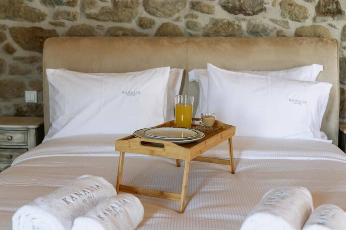 A bed with a tray holding a glass of orange juice, a plate, and a cup, with towels and pillows labeled 'Kanalia.'