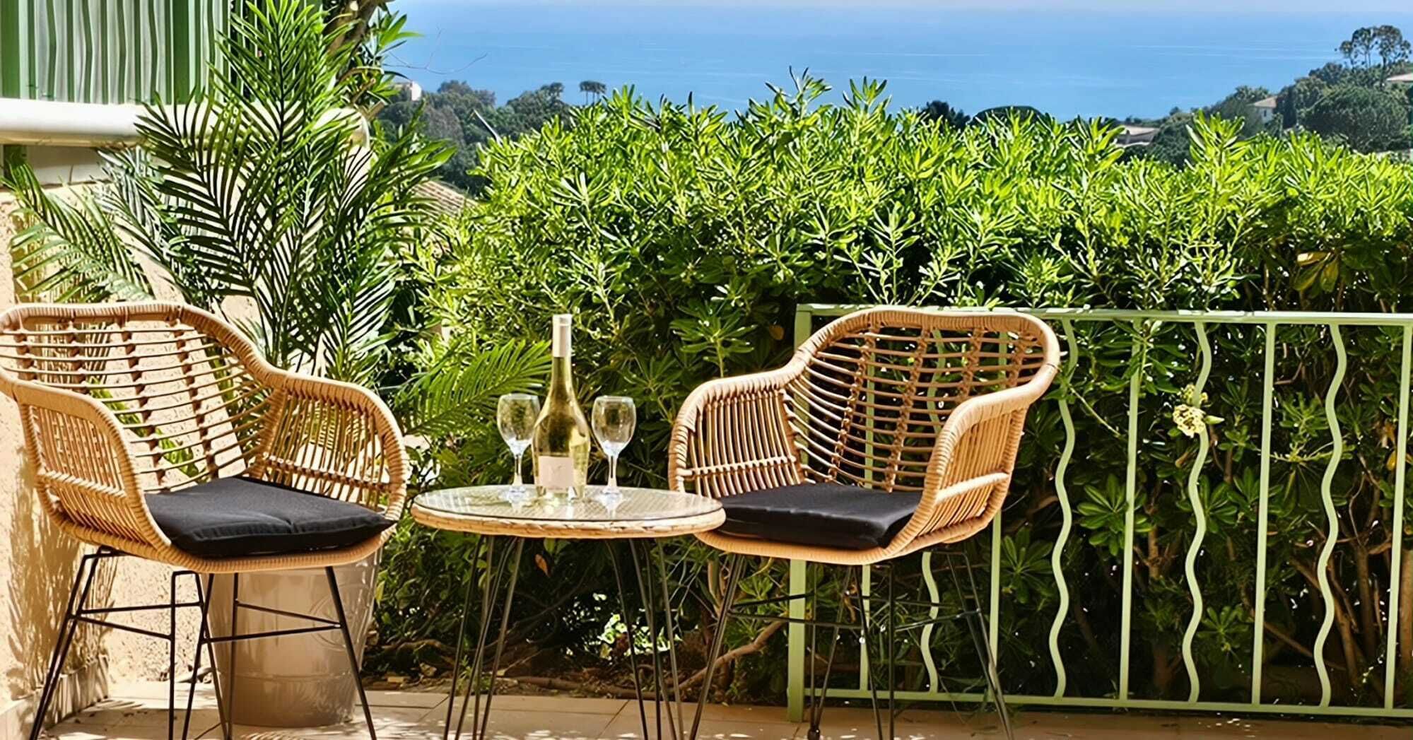 A wicker outdoor seating area with two chairs and a table, a bottle, and a glass.