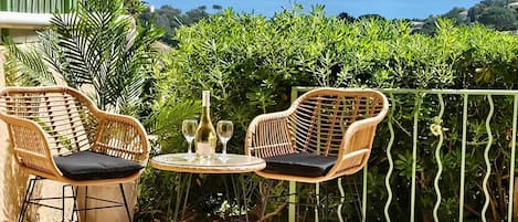 A wicker outdoor seating area with two chairs and a table, a bottle, and a glass.