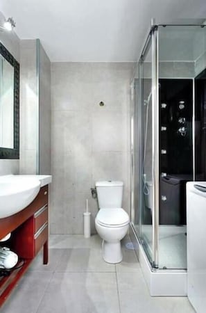 Un baño moderno con cabina de ducha de vidrio, inodoro blanco y tocador con espejo.