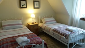A small, cozy bedroom with two single beds, a bedside table with a lamp, and a window with curtains.