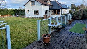 Ein zweigeschossiges Haus mit einem umzäunten Garten, einer Holzterrasse und Kübelpflanzen.