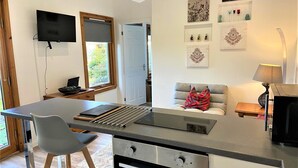 Eine moderne Küche mit Einbauofen, ein Essbereich mit Tisch und Stühlen, ein an der Wand befestigter Fernseher und ein Fenster mit Blick auf Grünflächen.