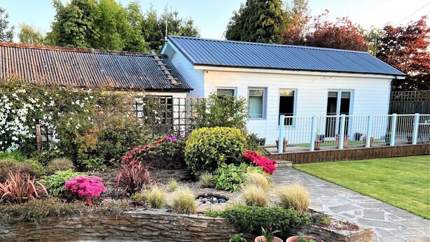 Ein Haus mit blauem Dach, ein Garten mit verschiedenen Pflanzen und Blumen sowie ein Kiesweg.