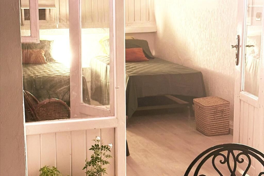 A room with two beds, a wicker chair, a small table, and a door leading to another room.
