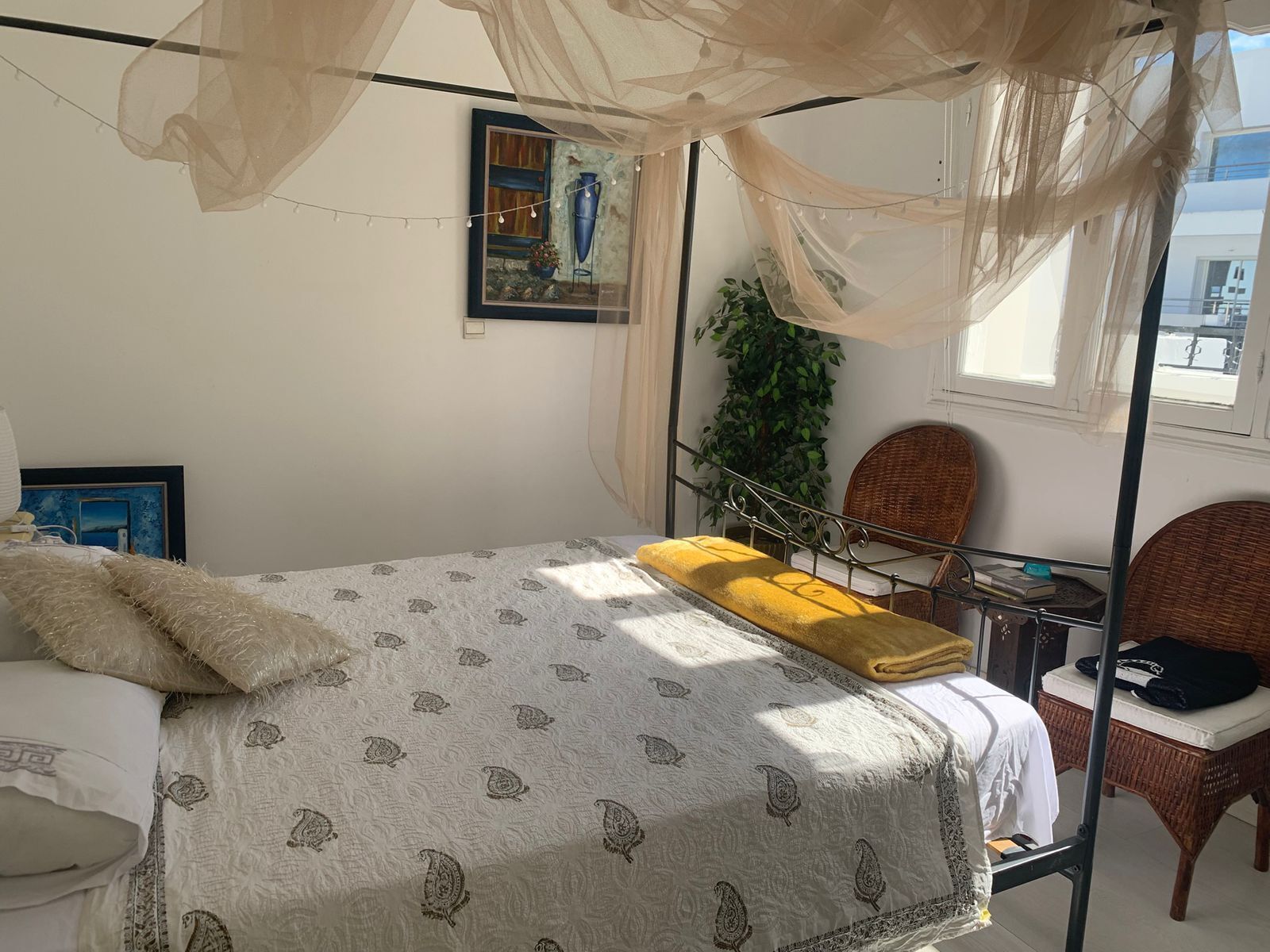 A bedroom with a four-poster bed, a chair, a small table, and a potted plant.