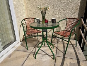 A green metal table with two wicker chairs, a vase with white flowers, and two patterned mugs on a textured wall. - 51 Llanteg Park (Narberth)