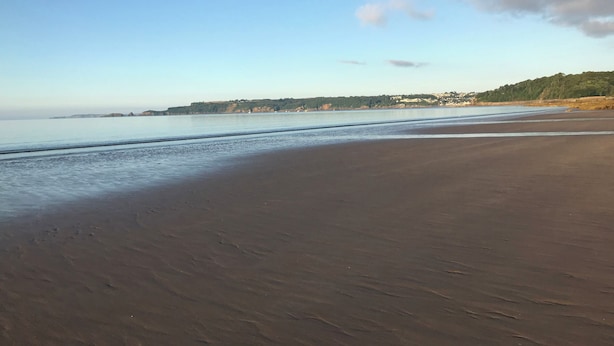 Een strand met een heldere lucht, rustig water en heuvels in de verte.