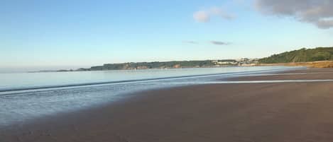 A beach with a clear sky, calm water, and distant hills.