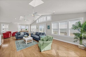 A spacious living room with a high ceiling, ceiling fans, and large windows with blinds. - Aqua Sea, a beachfront retreat (Carolina Beach)