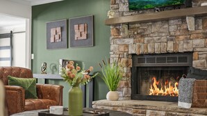 A living room with a stone fireplace, leather armchair, green walls, and a coffee table with a vase. - Stay@Black Sheep:Lakefront•HotTub•No Steps2Dock! Spacious_Location_Dog friendly (New Tazewell)