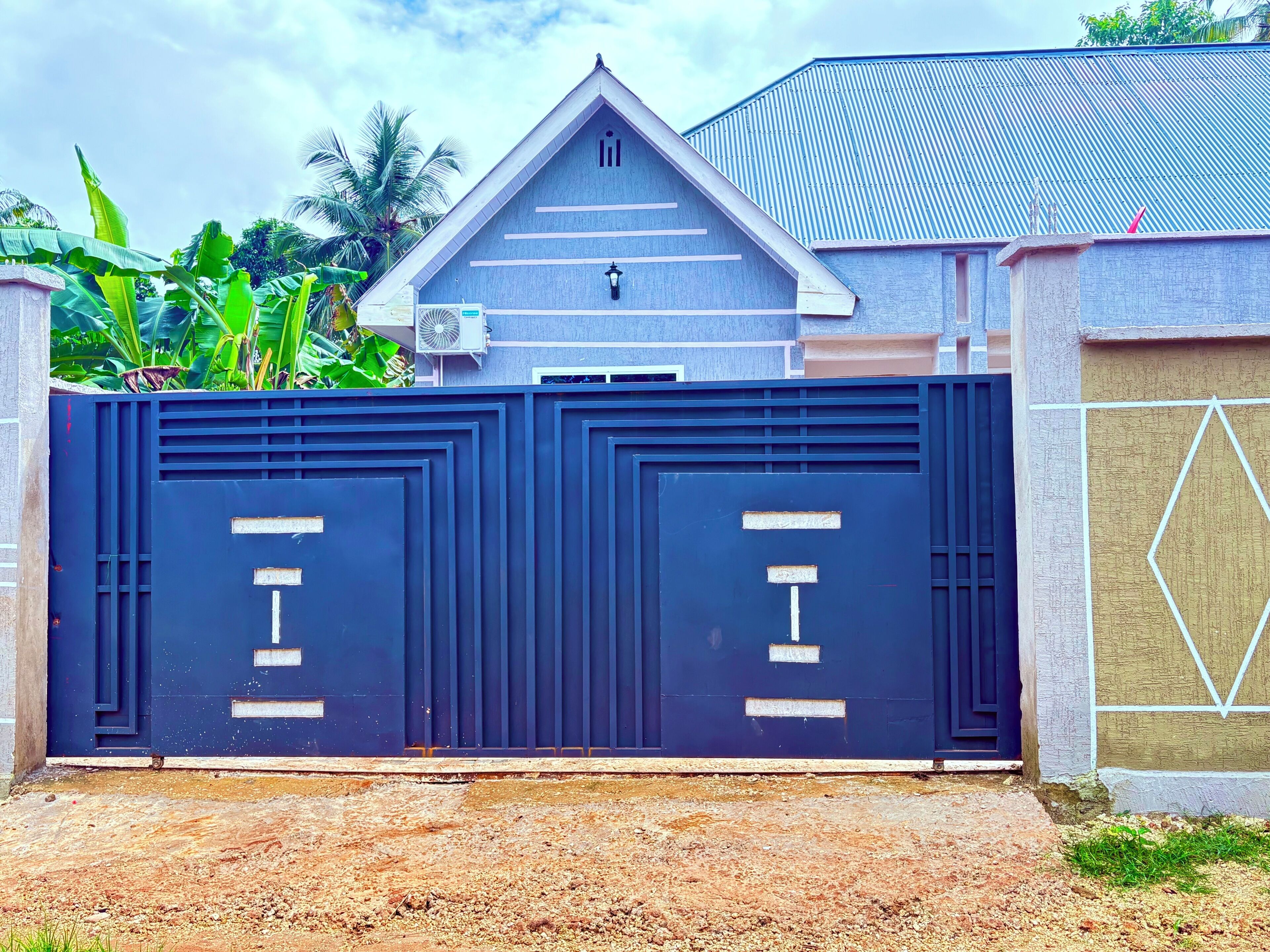 A gated entrance with a metal gate, a small overhang, and a wall with a geometric pattern.