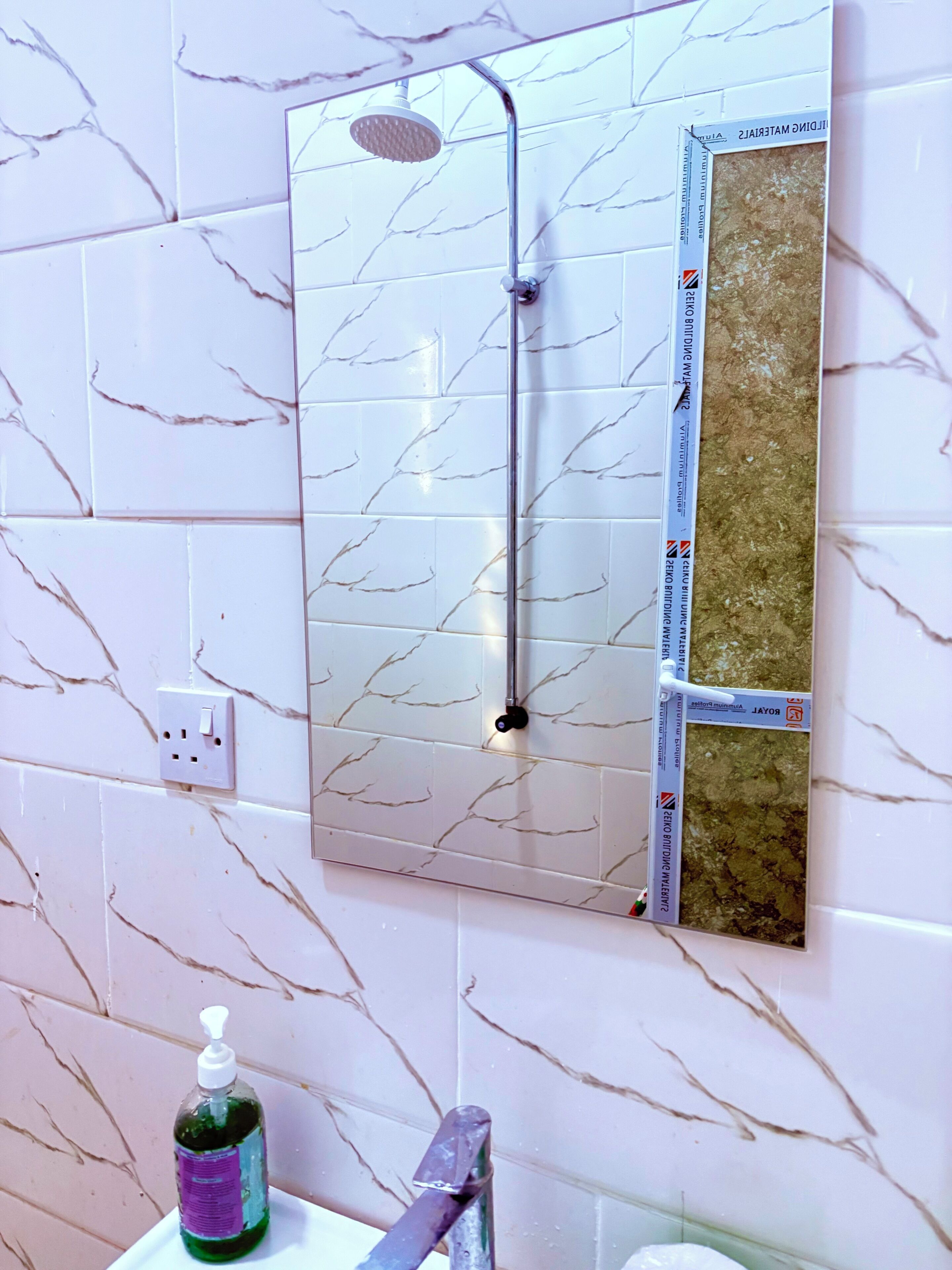 A bathroom with a shower, a mirror, and a soap dispenser.