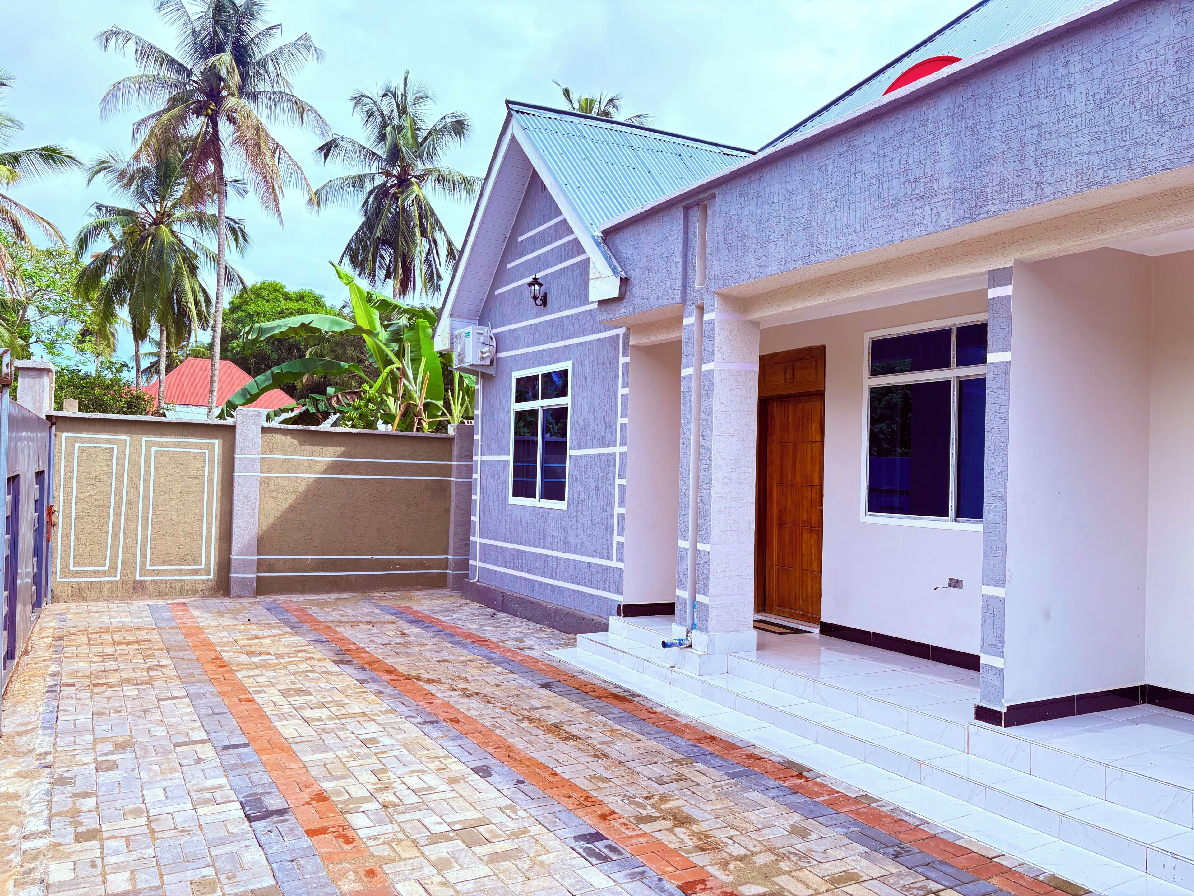 A house with a tiled patio, a gated entrance, and a small porch.