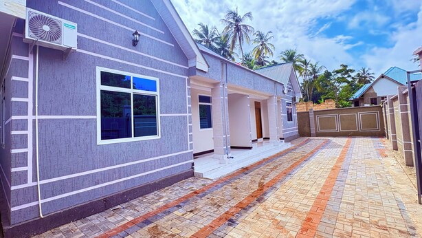 A residential building with a tiled driveway, a visible air conditioning unit, and a gated entrance.