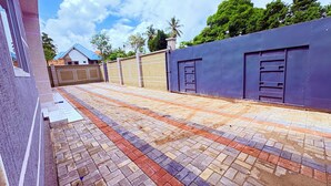 A paved courtyard with a patterned tile floor, a high wall with a gate, and a building with a blue roof in the background.