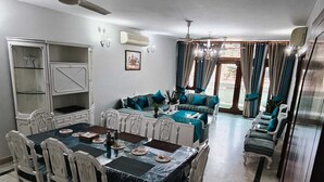 A dining area with a table set for four, a sofa set, a cabinet, and a ceiling fan. - South Delhi, Greater Kailash | 4 bedroom Private Apartment | Harmony Suites (New Delhi)