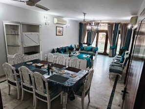 A dining area with a table set for four, a sofa set, a cabinet, and a ceiling fan.