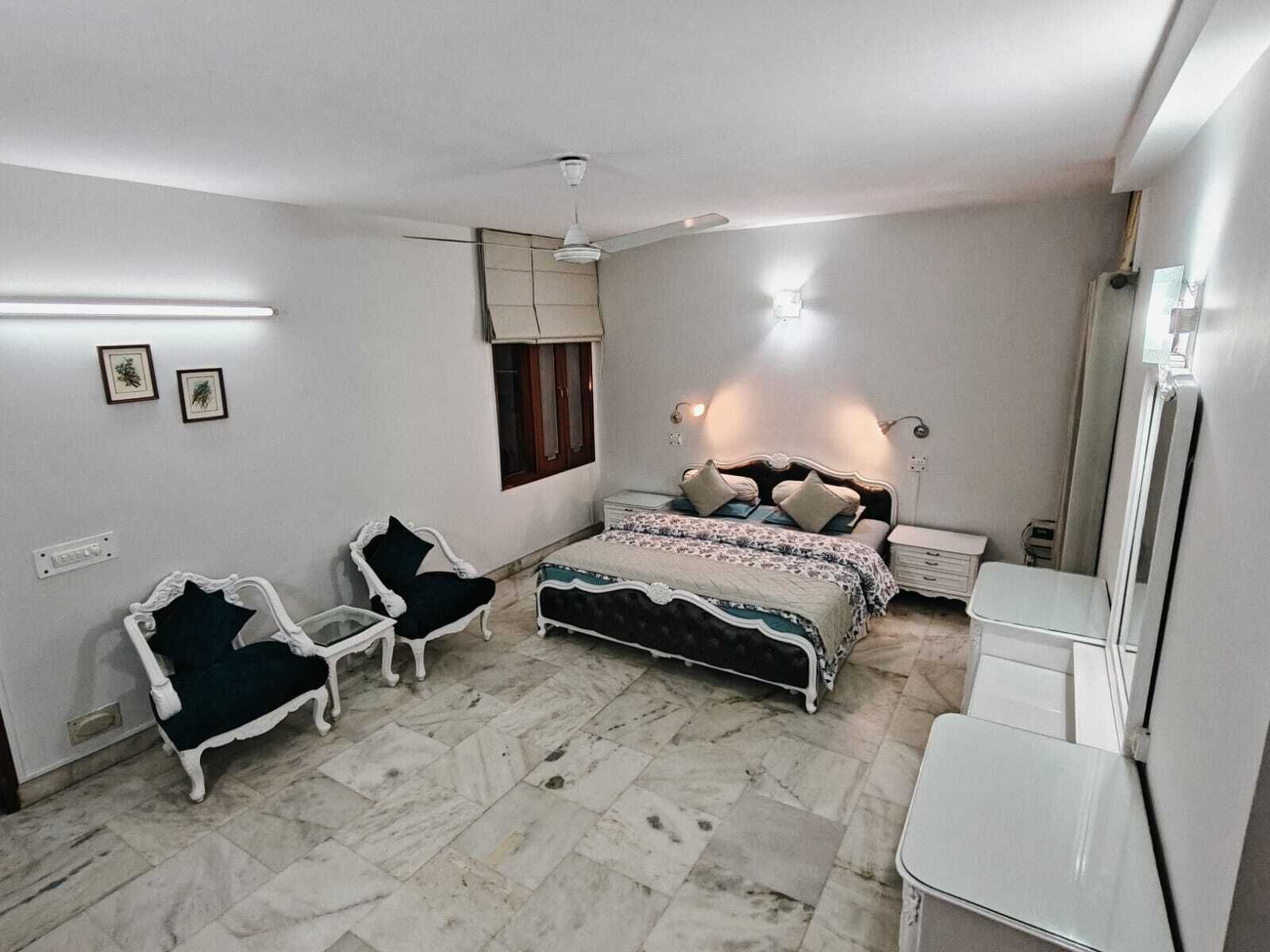 A bedroom with a bed, two chairs, a nightstand, a mirror, and a ceiling fan.