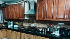 A kitchen with wooden cabinets, a black countertop, and various appliances including a microwave, stove, and coffee maker. - South Delhi, Greater Kailash | 4 bedroom Private Apartment | Harmony Suites (New Delhi)