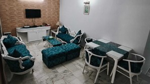 A living room with a TV, sofa, table, chairs, and a ceiling fan. - South Delhi, Greater Kailash | 4 bedroom Private Apartment | Harmony Suites (New Delhi)