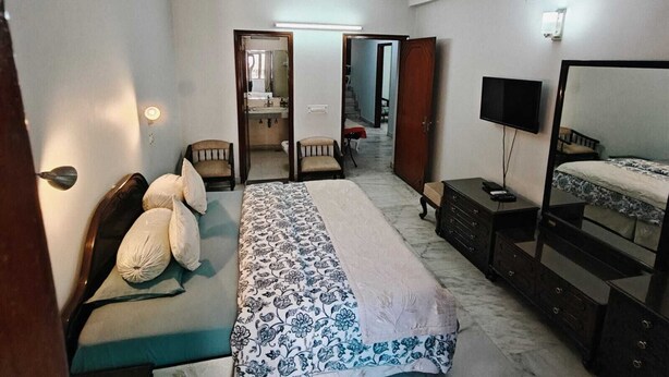 A bedroom with a bed, a TV, a dresser, and a ceiling fan. - South Delhi, Greater Kailash | 4 bedroom Private Apartment | Harmony Suites (New Delhi)