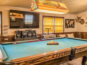 A pool table with speakers, a television, and a mounted deer head.