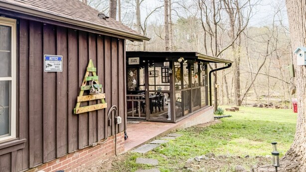 A wooden building with a covered patio area, a Christmas tree decoration, and a sign indicating 24-hour surveillance. - Almeneiro Cabin - A Charming Nature Retreat (Greensboro)