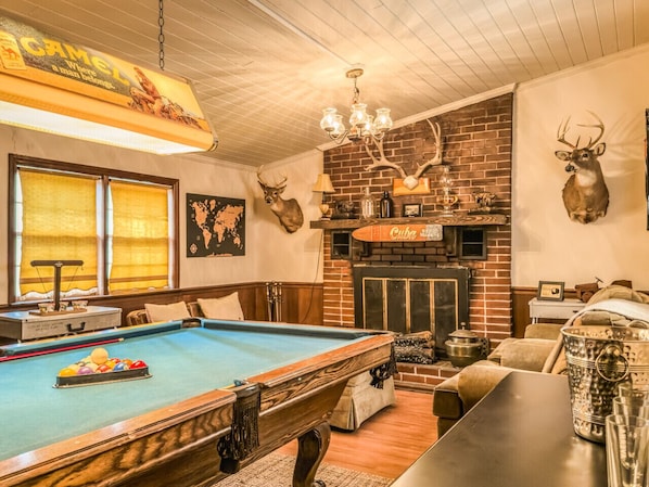 A pool table with a billiard cue, a fireplace, and deer antlers on the wall.