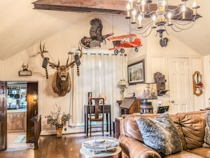A cozy living room with a fireplace, a chandelier, and various hunting trophies on the wall.