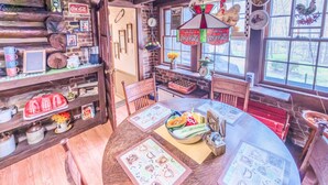 A rustic dining area with a wooden table, chairs, and a variety of items on the shelves, including a Coca-Cola sign and a rooster decoration. - Almeneiro Cabin - A Charming Nature Retreat (Greensboro)
