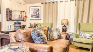 A living room with a brown leather sofa, a green armchair, and a round coffee table. - Almeneiro Cabin - A Charming Nature Retreat (Greensboro)