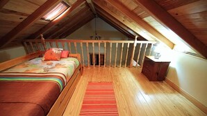 An attic bedroom with a wooden ceiling, a bed with a colorful bedspread, a red rug, and a wooden dresser.