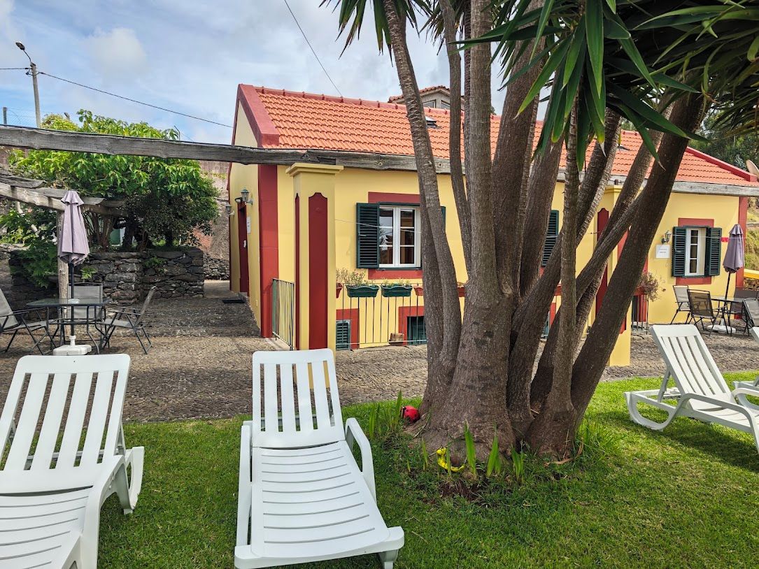 A yellow building with a red roof, white lounge chairs, and a palm tree.
