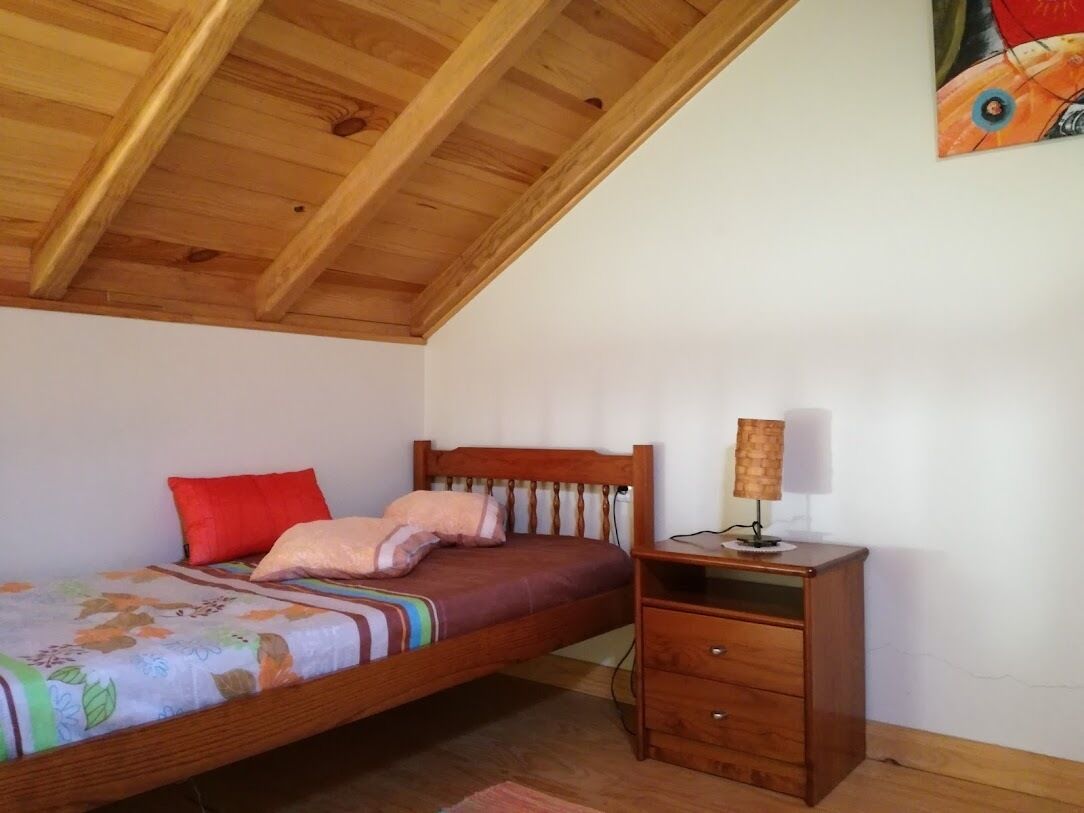 Ein Schlafzimmer mit Holzboden, einem Bett mit floralem Bettbezug, einem Nachttisch mit Lampe und einer kleinen Kommode.