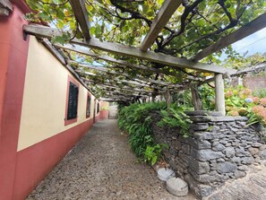 Un sentiero in pietra che conduce a un edificio con una pergola in legno e un muro in pietra.