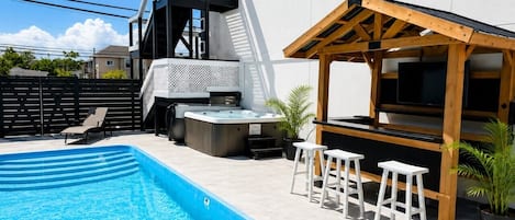 Una piscina con hidromasaje, mobiliario exterior y una pérgola.