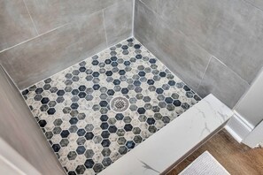 Eine Dusche mit sechseckigen Fliesen in Grau- und Weißtönen, einem zentralen Abfluss und einer weißen Marmorarbeitsplatte.