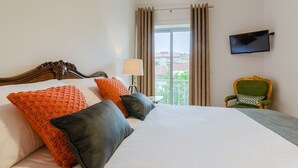 Habitación de hotel con una cama grande, un televisor montado en la pared, una silla y vistas a la ciudad desde la ventana.