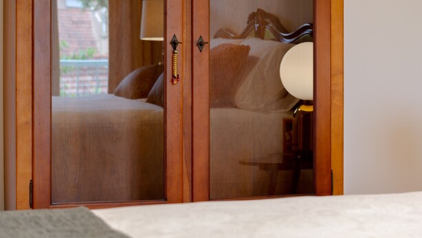 Un dormitorio con un armario de madera, una cama con cabecera blanca y una lámpara de noche.