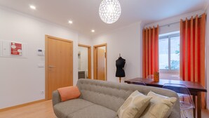 Una sala moderna con un sofá gris, una puerta de madera, un maniquí y un comedor con mesa y sillas.
