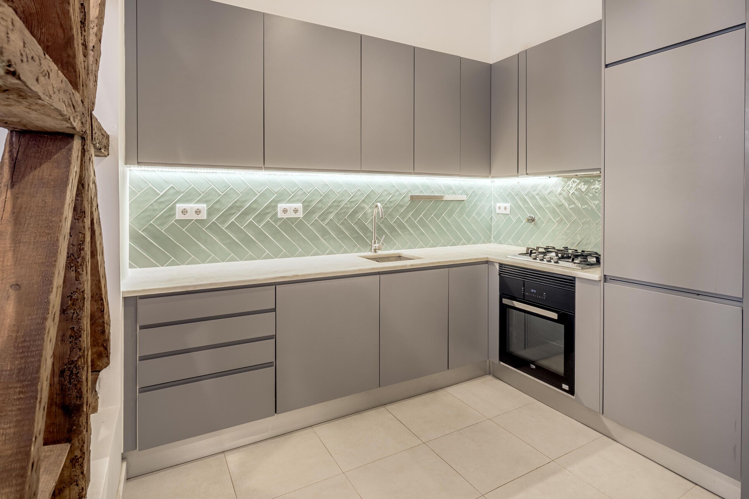A modern kitchen with grey cabinets, a herringbone tile backsplash, and a built-in oven.