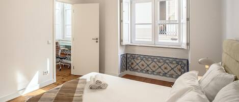 A bedroom with a bed, a window with a view, a door leading to another room, and a wall-mounted air conditioner.