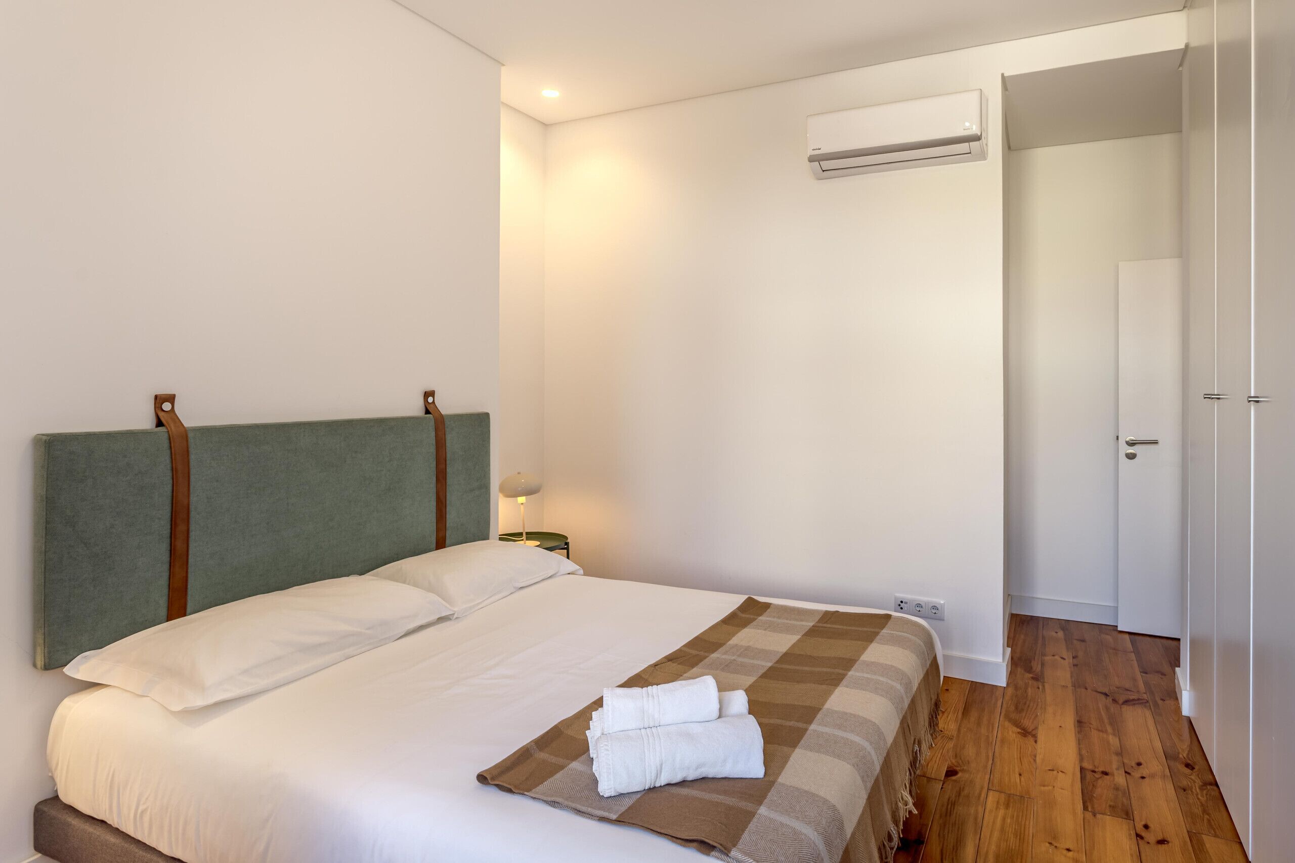 A neatly made bed with a headboard, a bedside lamp, and a folded towel on the bed.